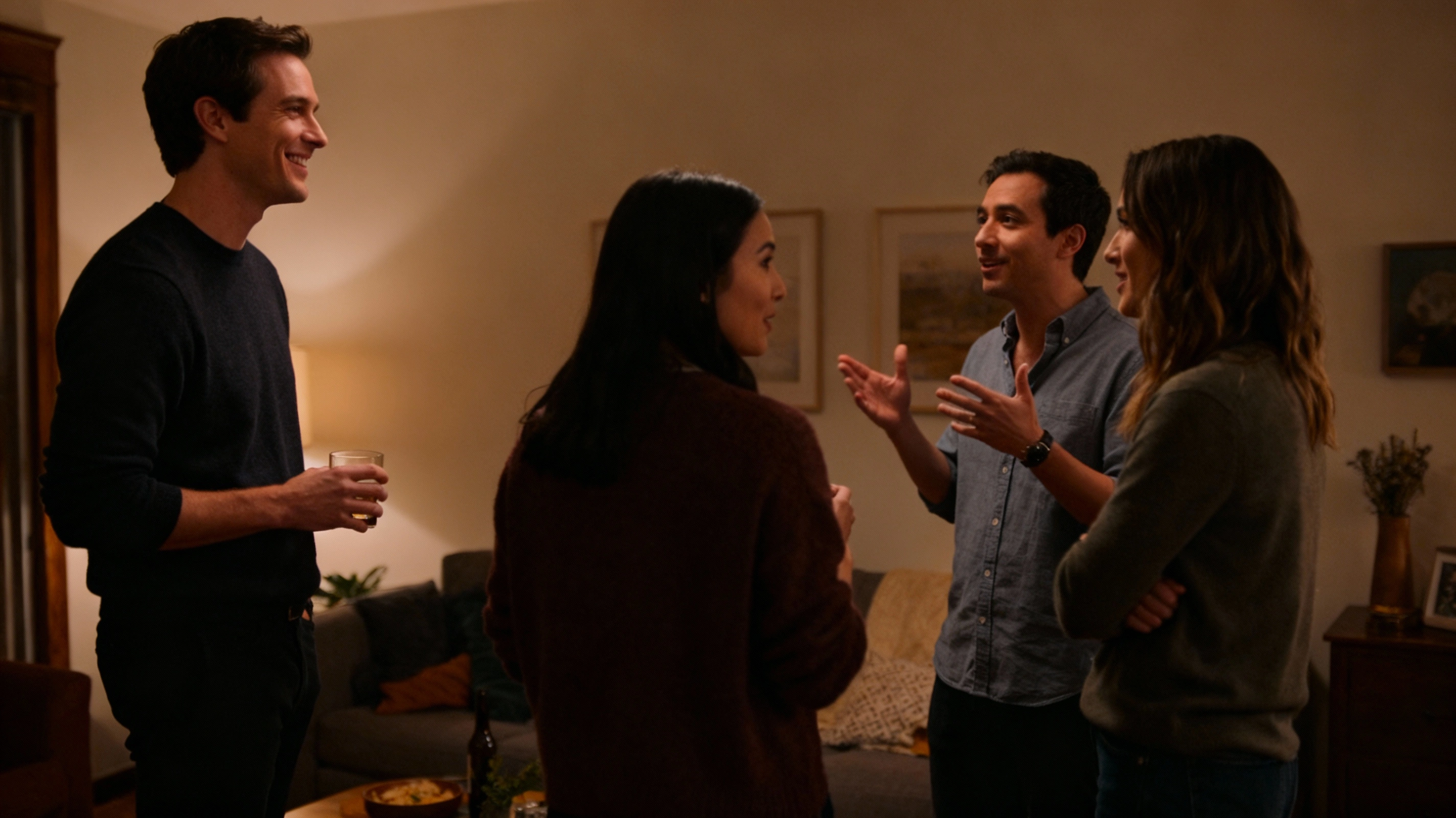 small group talking at a casual house party, introvert guy listening and smiling at the edge of the circle
